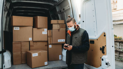 Delivery man is checking his smart phone in front of the delivery van. He's wearing a protective face mask. Dummy QR code and barcode.